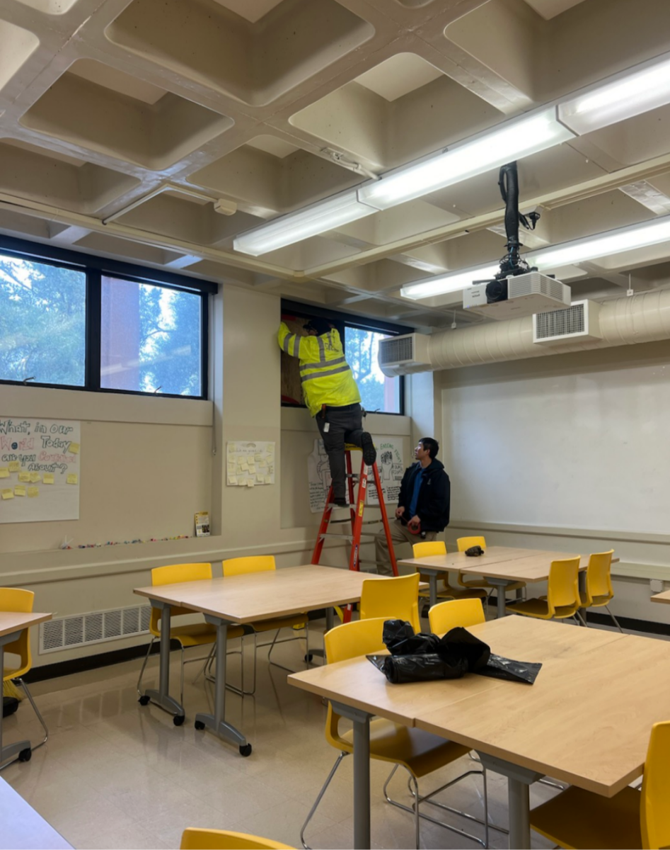 Maintenance workers cover the broken window with plywood in Building 8, Room 8-118.