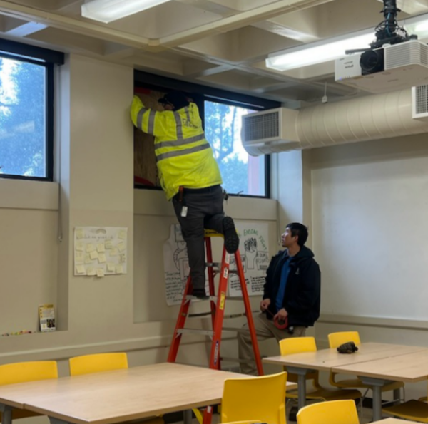 Maintenance workers cover the broken window with plywood in Building 8, Room 8-118.