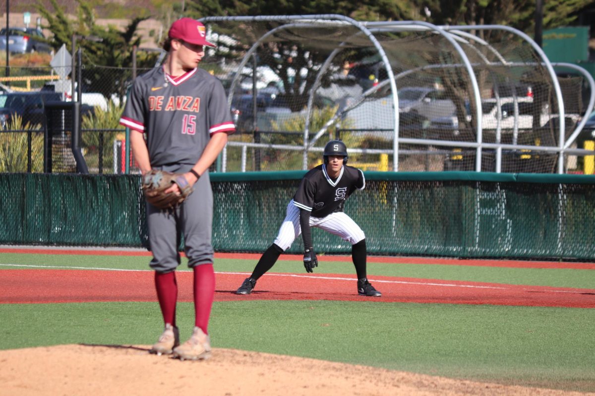 De Anza freshman pitcher Chris Smith (left) on the mound as Skyline freshman outfielder Vinny Smith (center) takes his lead at first base.